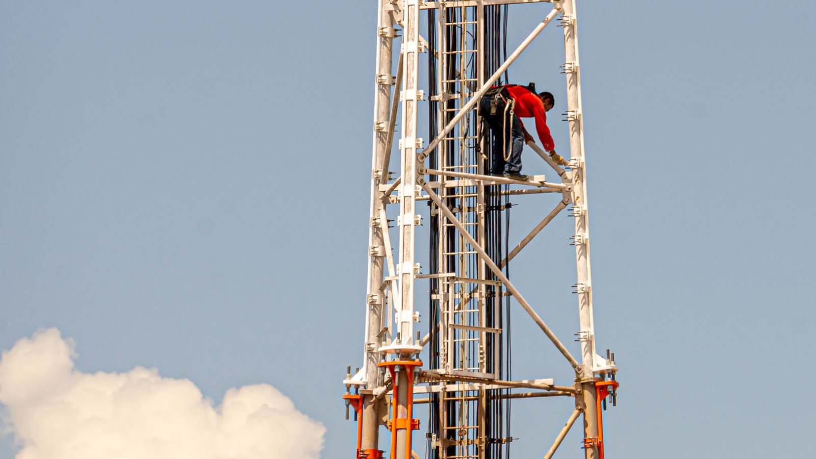 A technician working high up on a broadcast tower against a blue sky