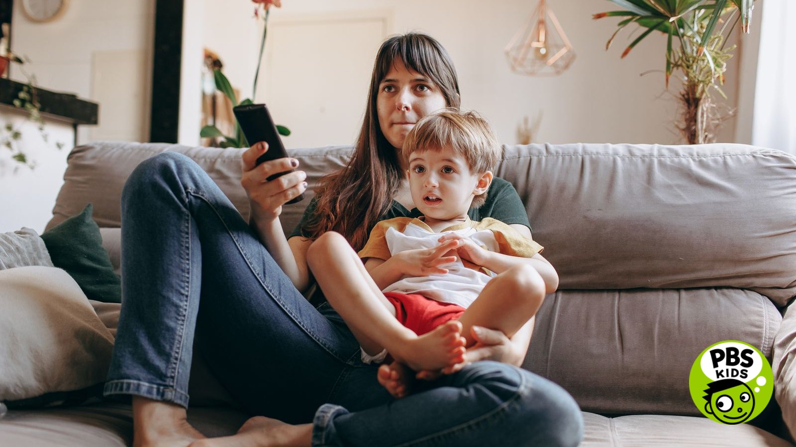 A parent and young child watching television together on a sofa at home