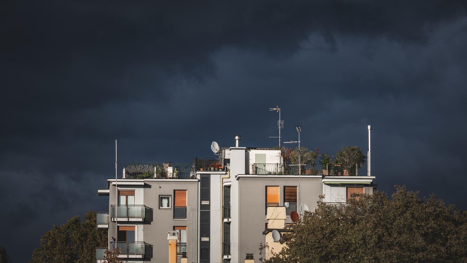 Rooftop TV antennas and satellite dishes against a dark storm sky